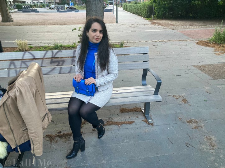 A beige skirt suit in French tweed worn with black accessories and an azure blue turtleneck and bag.