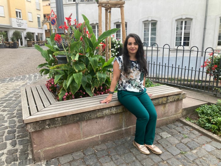 Green business pants combined with a white blouse with roses and leafs on it, a green cross body bag and golden accessories make the perfect urban jungle look.