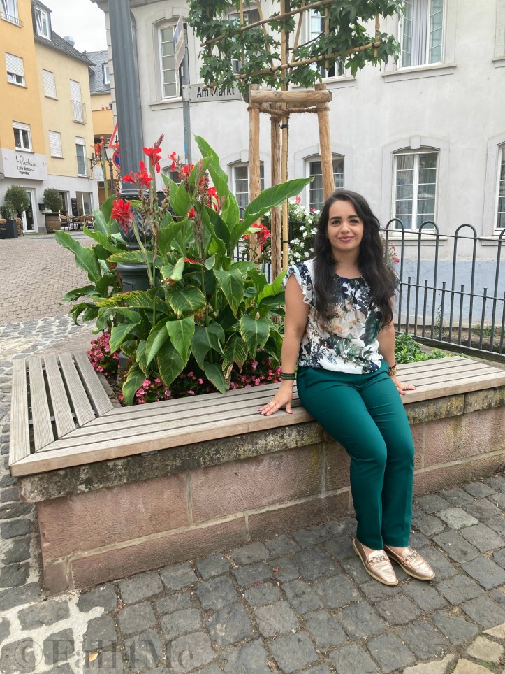Green business pants combined with a white blouse with roses and leafs on it, a green cross body bag and golden accessories make the perfect urban jungle look.