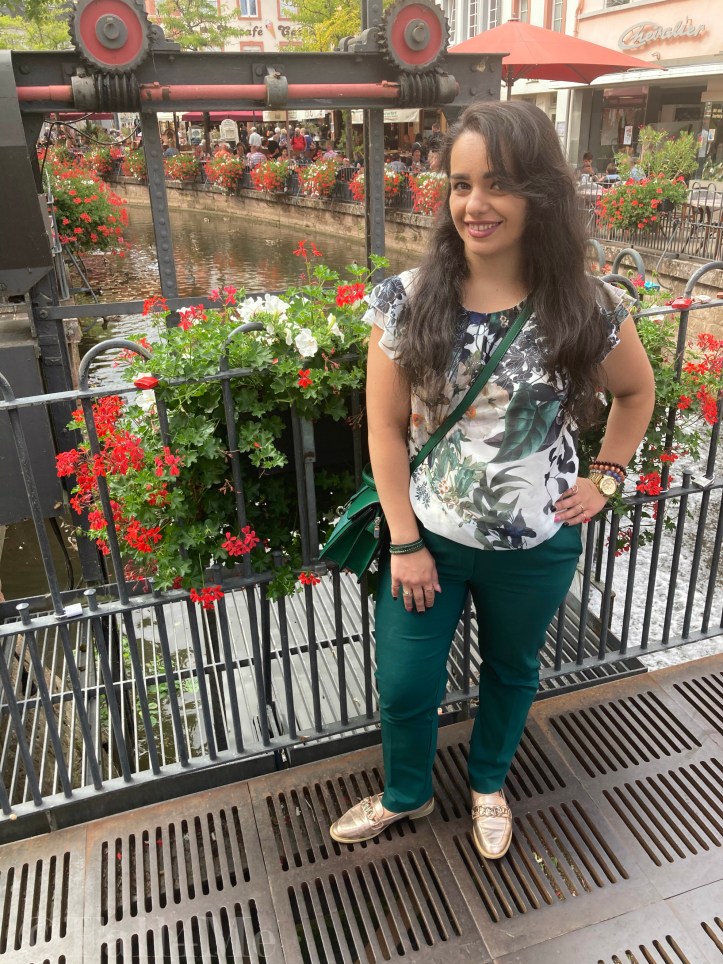 Green business pants combined with a white blouse with roses and leafs on it, a green cross body bag and golden accessories make the perfect urban jungle look.