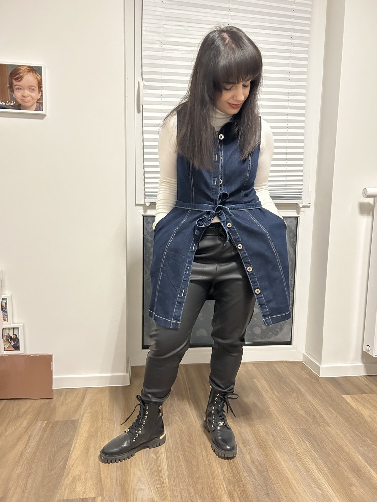 An oversized denim vest worn with a white turtleneck, filigree black combat boots and faux-leather jogpants.