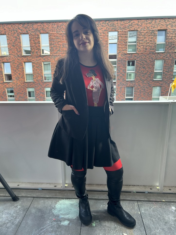 A pleated skirt making the skirt of the season worn with a black blazer, black over-knee-boots and red tights.