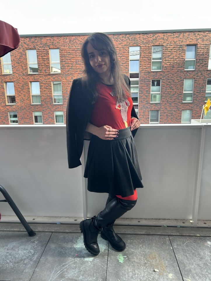 A pleated skirt making the skirt of the season worn with a black blazer, black over-knee-boots and red tights.