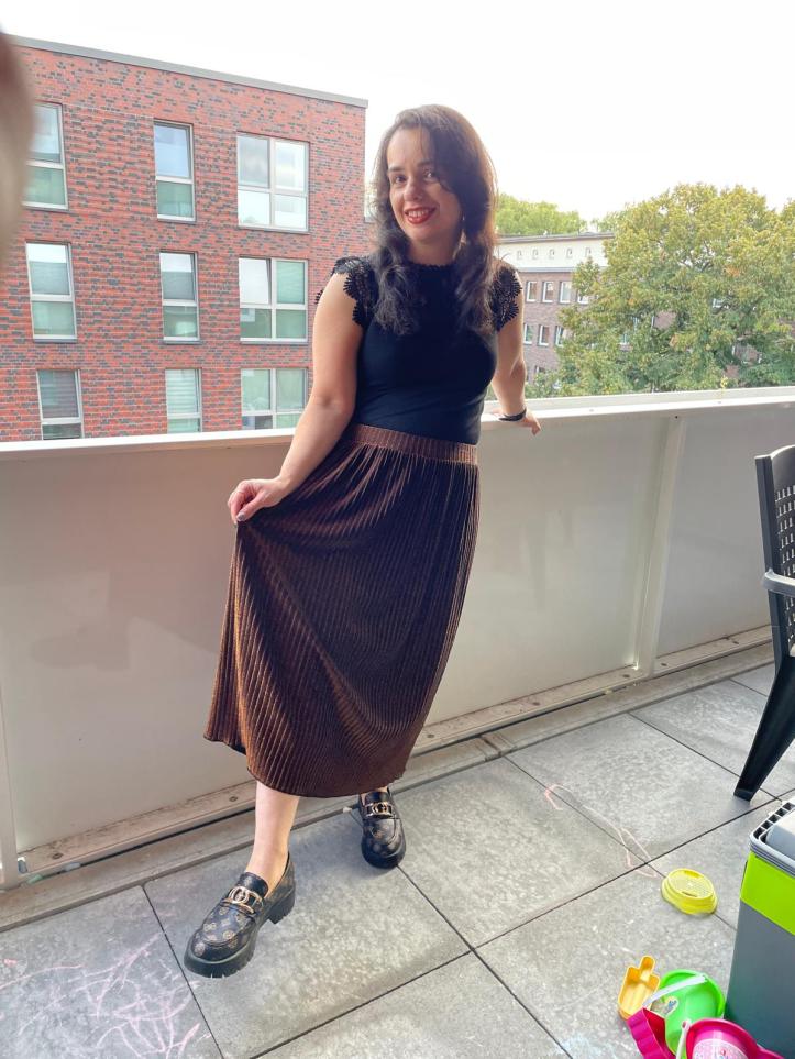 A gold-glitter pleated skirt worn with a black shirt and black/brown loafers