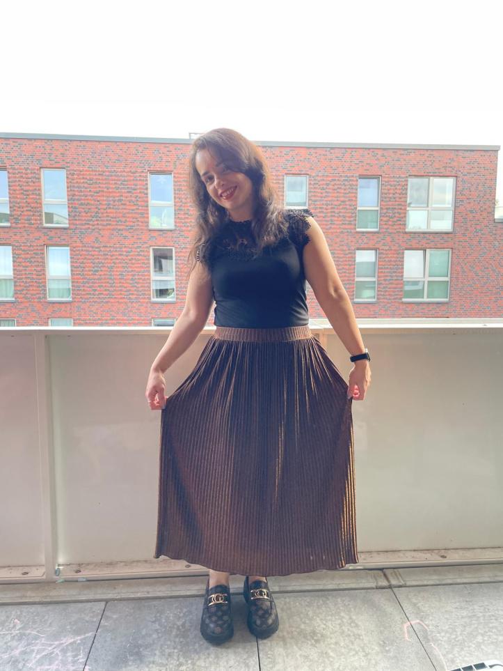 A gold-glitter pleated skirt worn with a black shirt and black/brown loafers