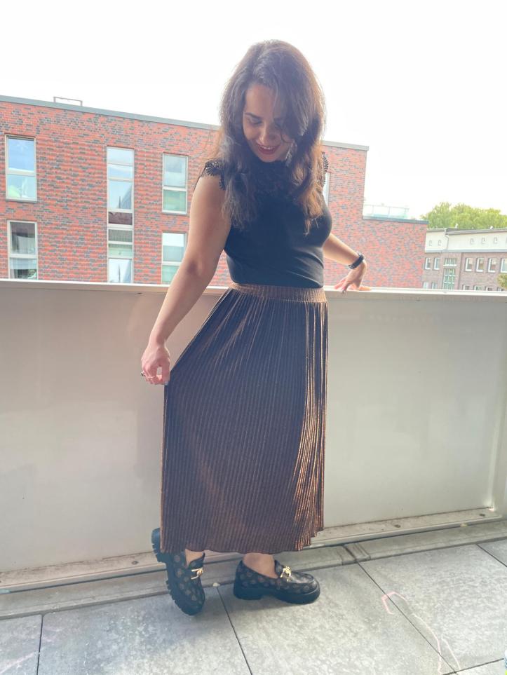 A gold-glitter pleated skirt worn with a black shirt and black/brown loafers